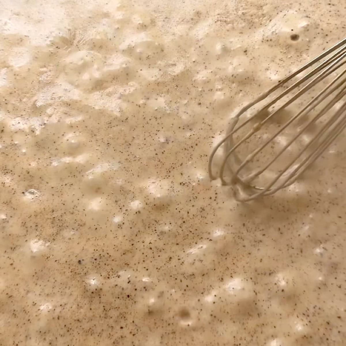 Creamy gravy being whisked in a cast iron skillet.