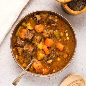 Dutch oven beef stew next to linen, black pepper, and a wooden spoon.