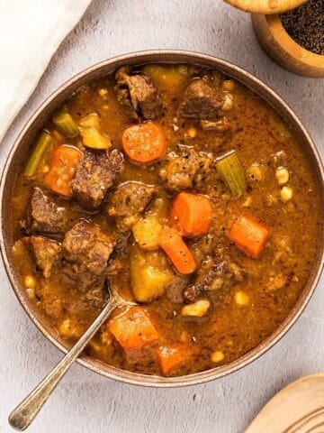 Dutch oven beef stew next to linen, black pepper, and a wooden spoon.