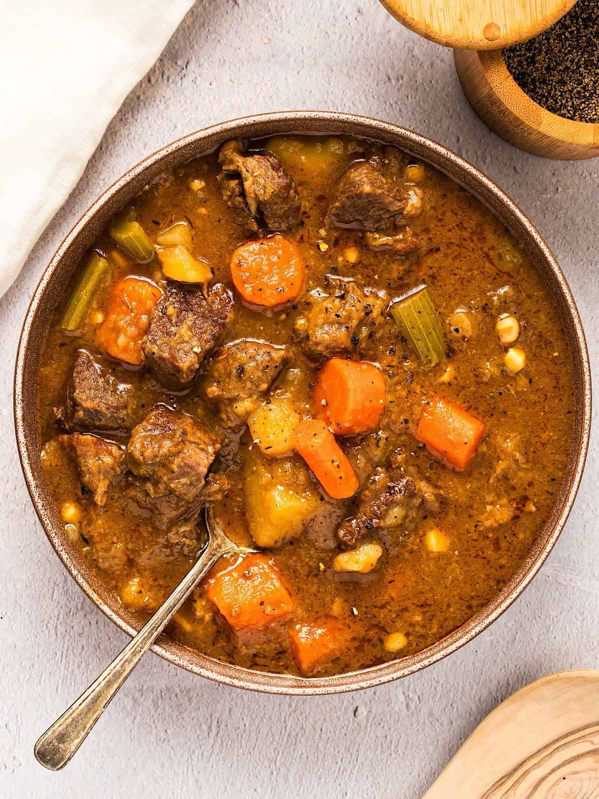 Dutch oven beef stew next to linen, black pepper, and a wooden spoon.