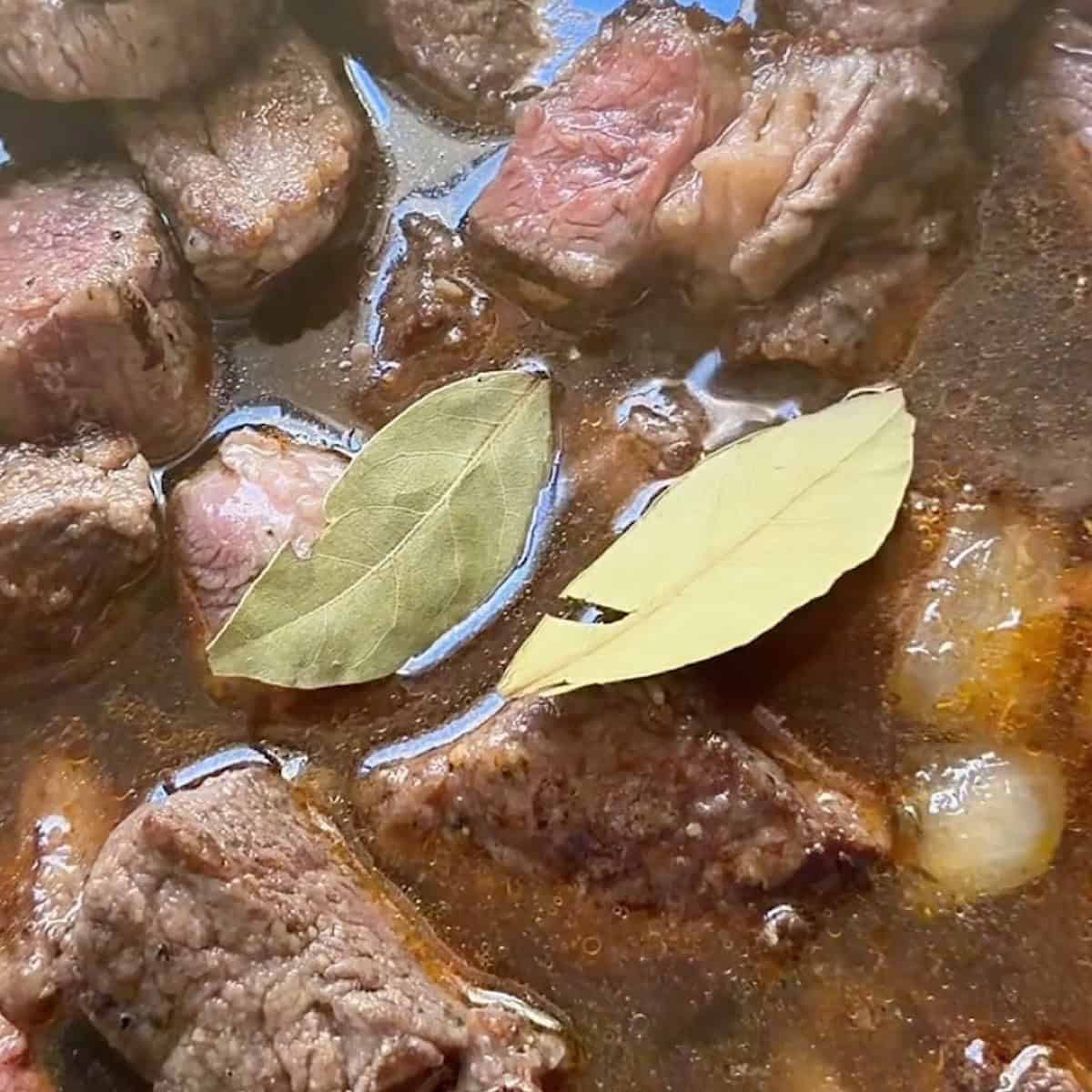 Simmering the beef in broth and seasoning with bay leaves.