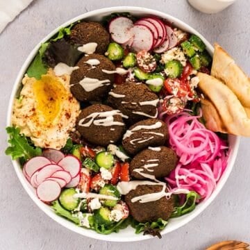Falafel salad in a large wide bowl with lemon tahini dressing drizzled over the top.