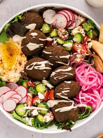 Falafel salad in a large wide bowl with lemon tahini dressing drizzled over the top.