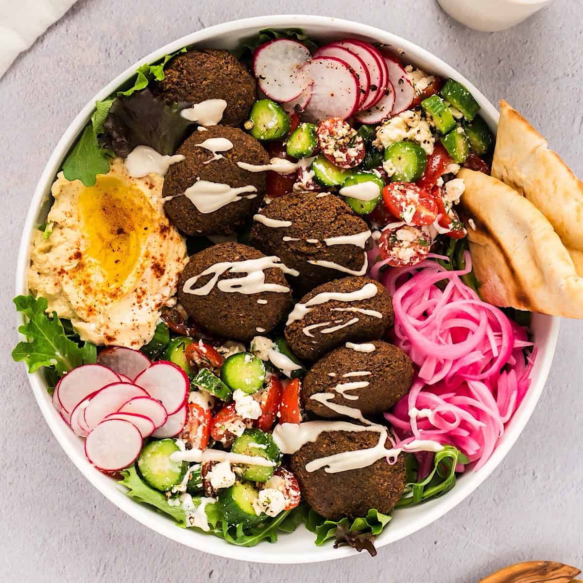 Falafel salad in a large wide bowl with lemon tahini dressing drizzled over the top.