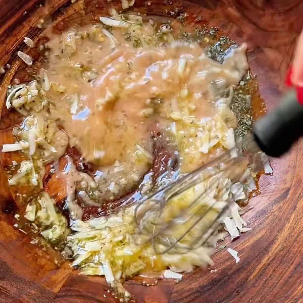 Whisking the red wine vinaigrette in a bowl with parmesan.