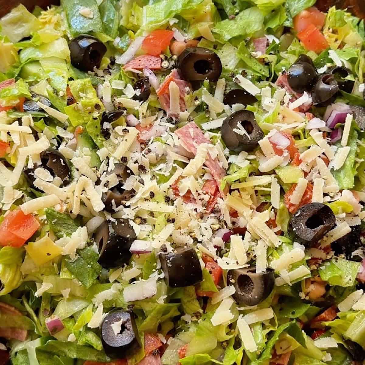 A tossed chopped italian grinder style salad in a wooden bowl ready to serve.