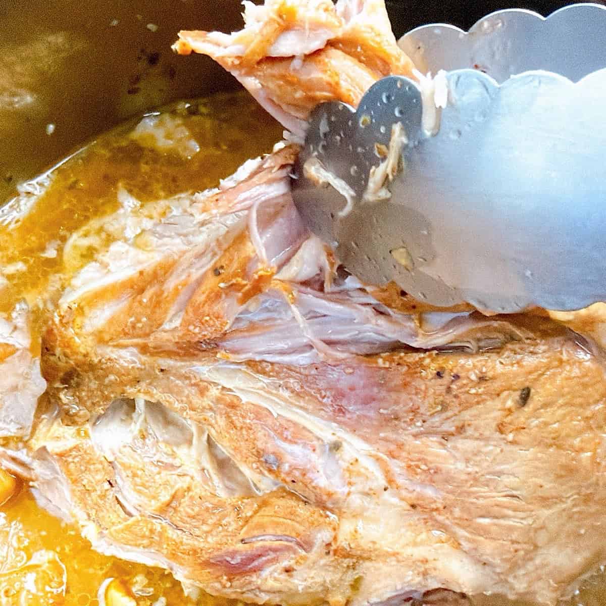 Using tongs to show how easily the pork lifts from the bone.