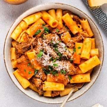 A wide bowl of beef rigatoni for serving with parmesan, linen, etc for composition.