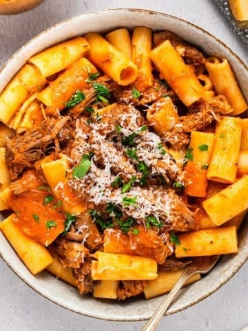 A wide bowl of beef rigatoni for serving with parmesan, linen, etc for composition.