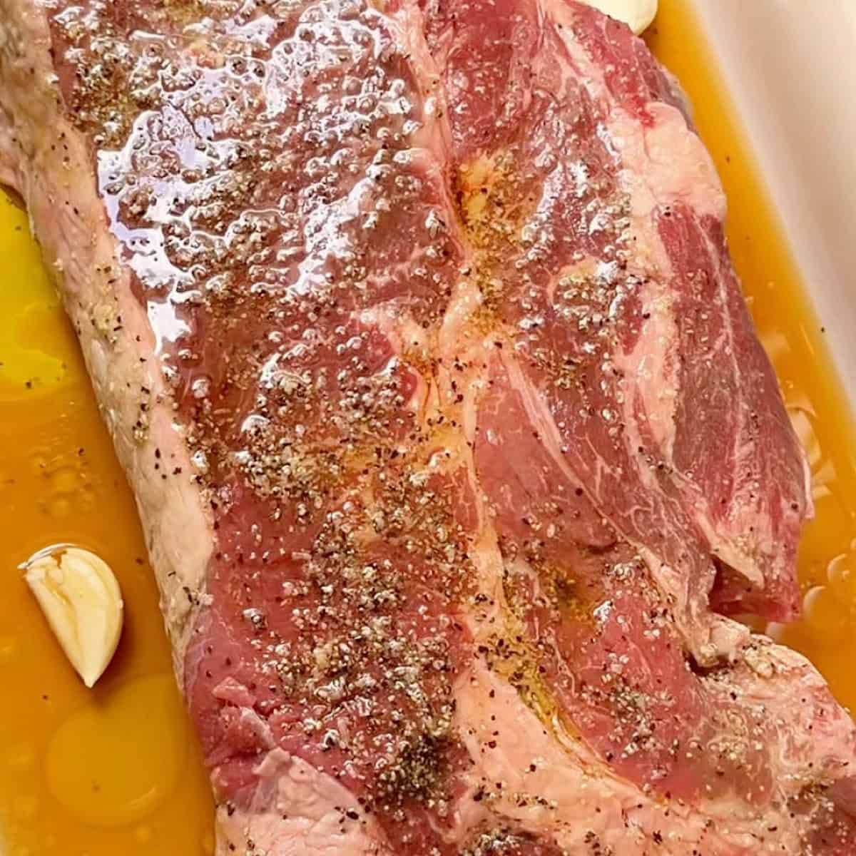 Prepared chuck roast with oil, seasoning, and beef broth ready to bake.
