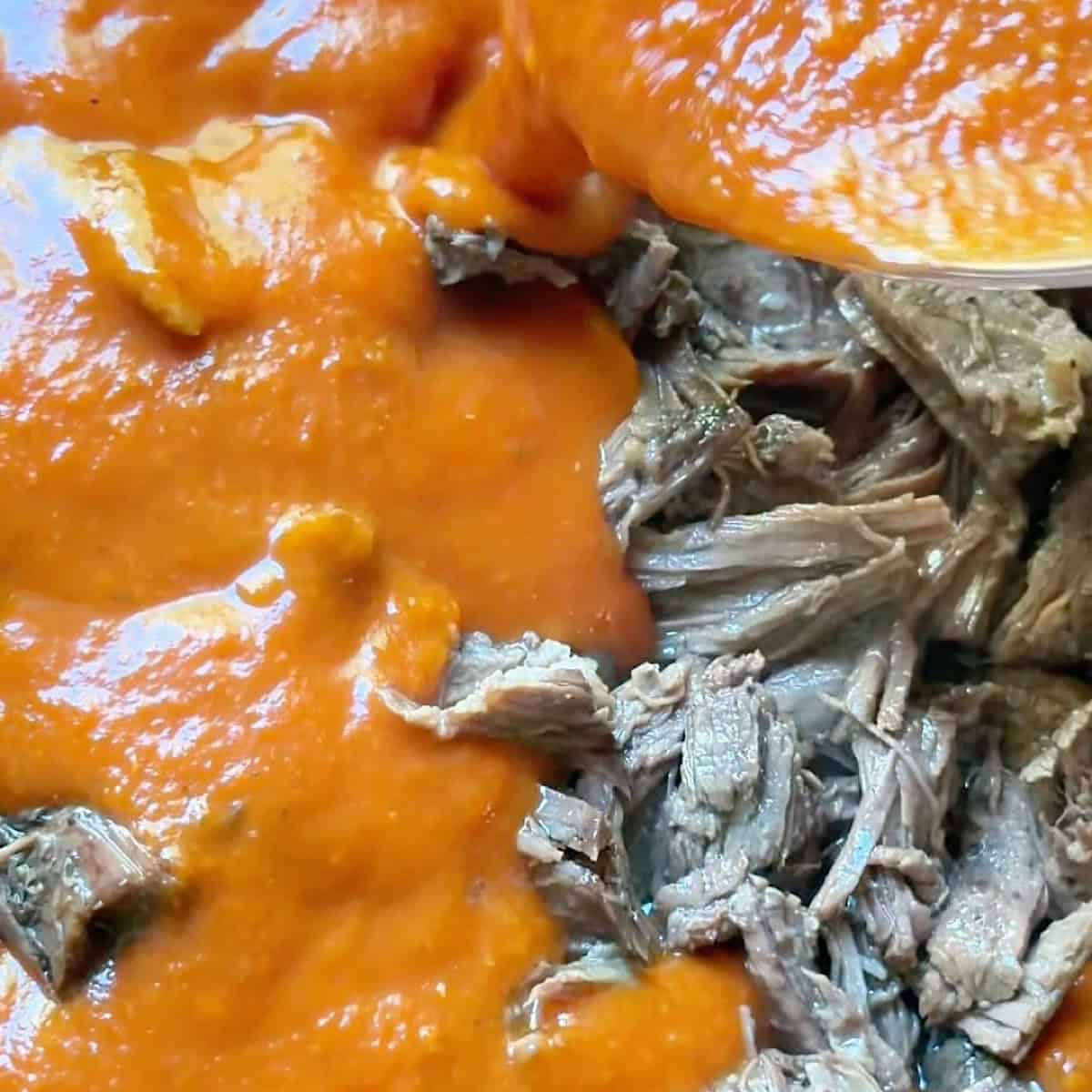 Pouring marinara sauce over the shredded beef and juices.