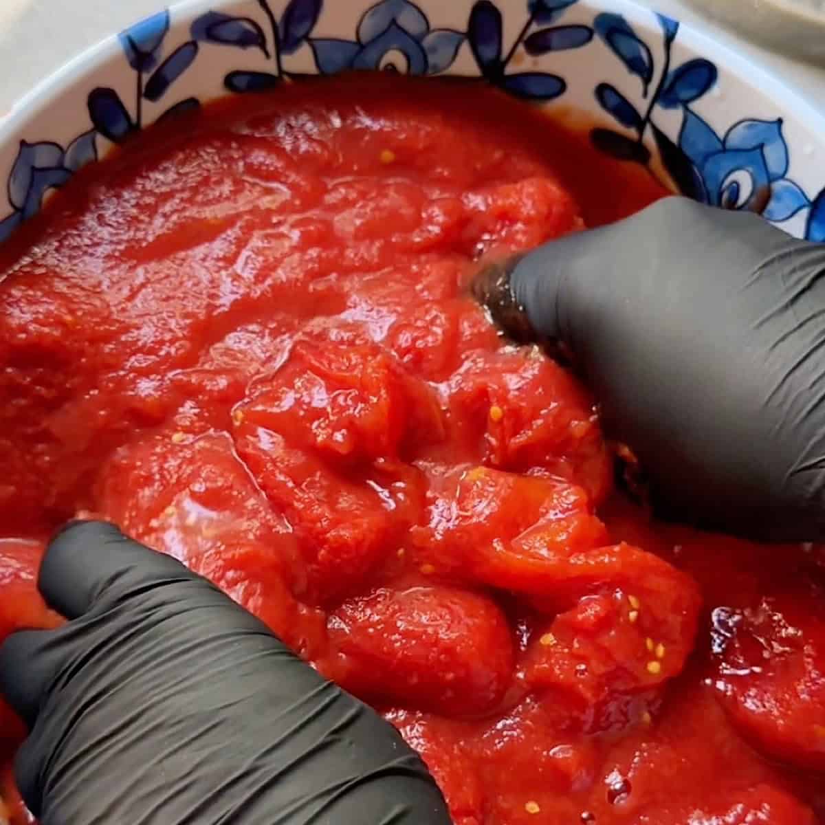 Crushing San Marzano tomatoes by hand with gloves on.