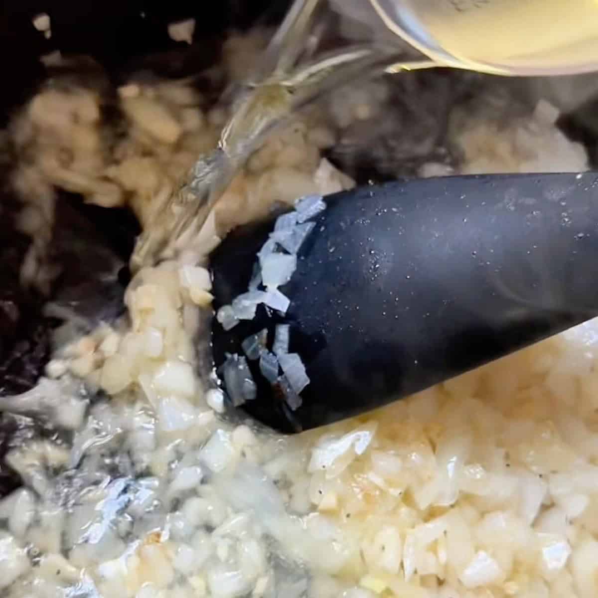 Adding white wine to the translucent onions to deglaze.