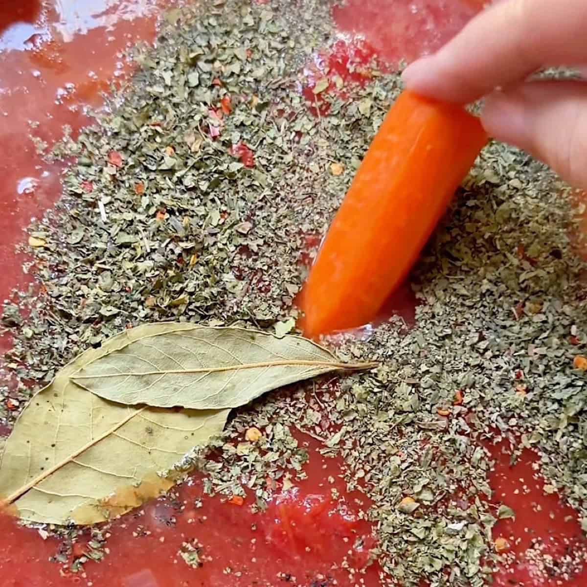 Adding a carrot to the tomatoes and seasoning.