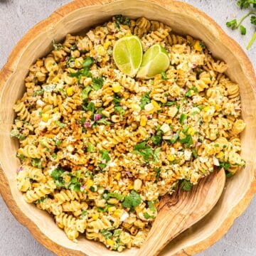 Elote pasta salad in a wooden bowl with a serving spoon and lime cilantro garnish.