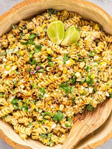 Elote pasta salad in a wooden bowl with a serving spoon and lime cilantro garnish.