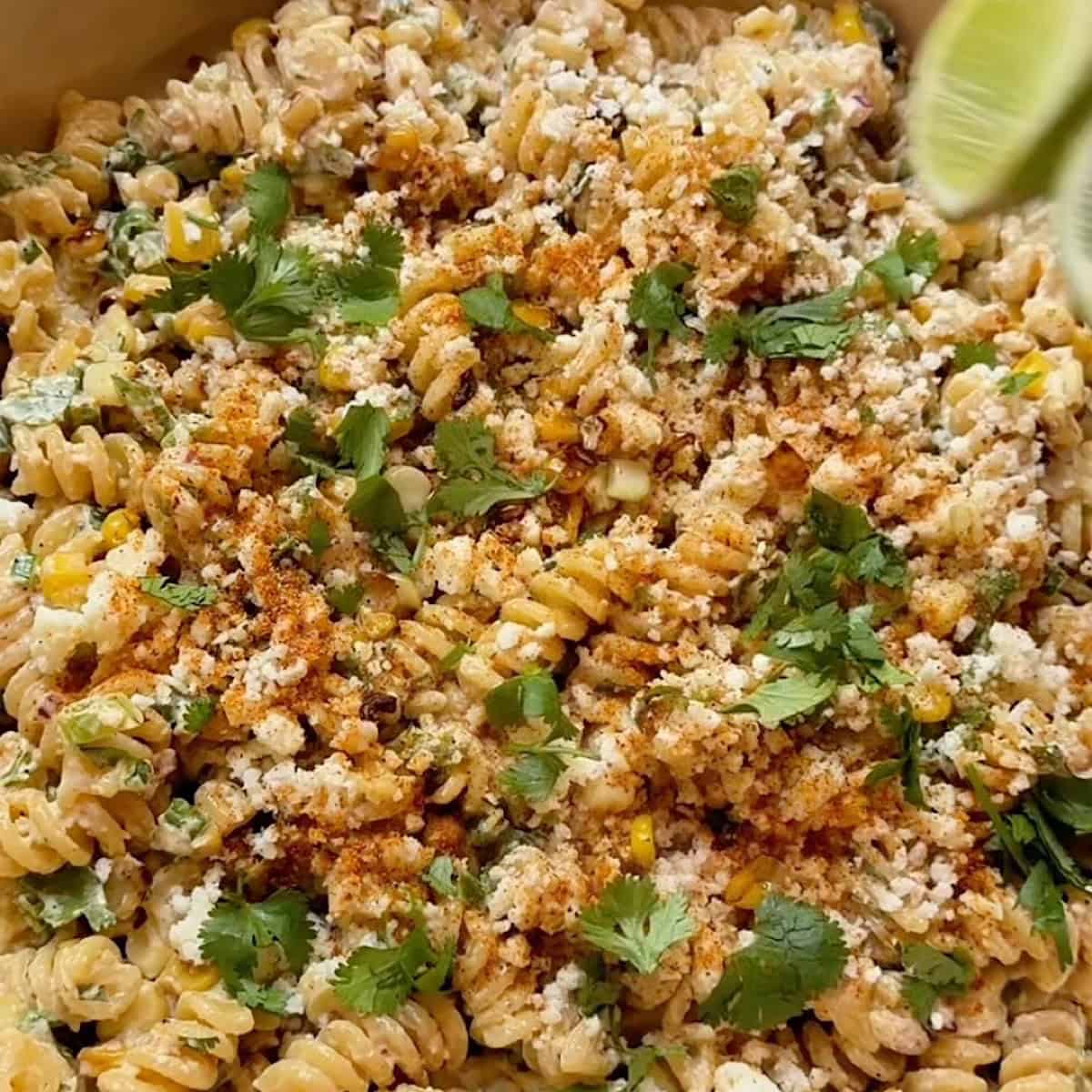 Elote corn pasta salad in a wide bowl with cotija, elote seasoning, and cilantro for garnish.