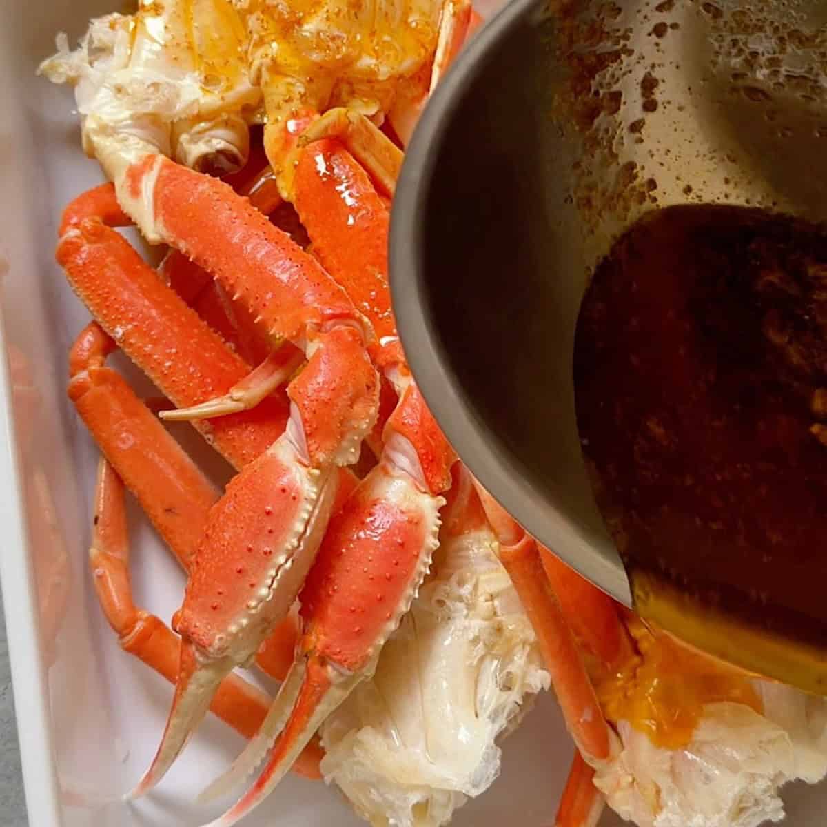 Pouring cajun garlic butter over crab legs in a baking dish.