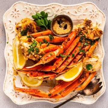 An elegant plate full of snow crab legs, lemon wedges, parsley, and garlic butter.