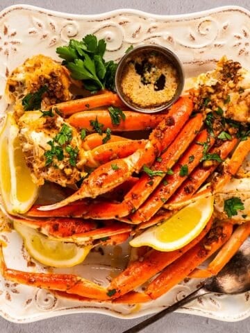 An elegant plate full of snow crab legs, lemon wedges, parsley, and garlic butter.