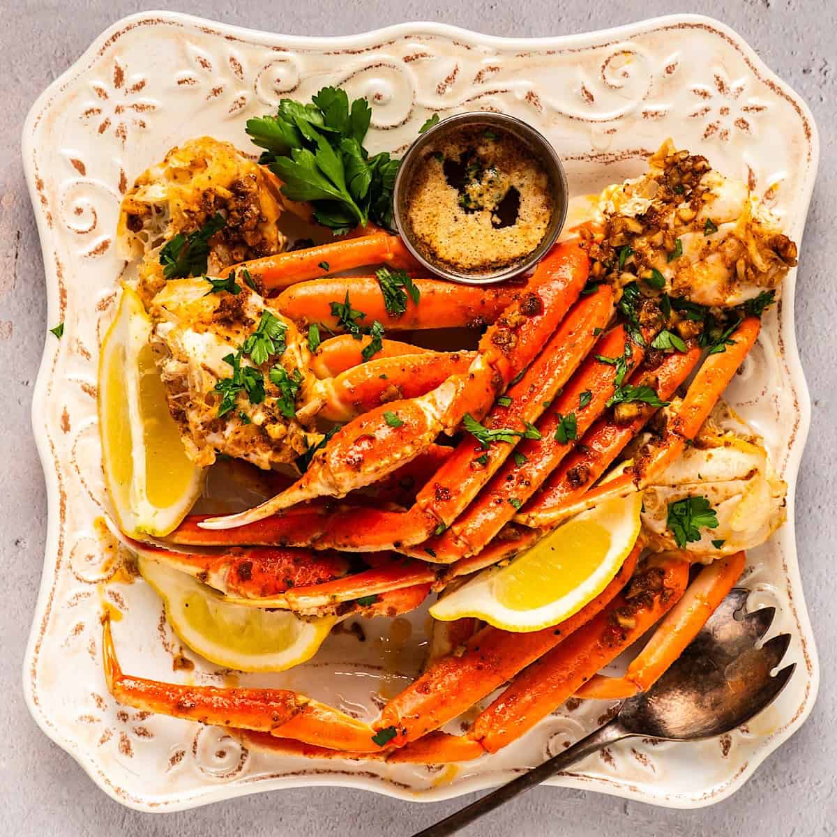 An elegant plate full of snow crab legs, lemon wedges, parsley, and garlic butter.
