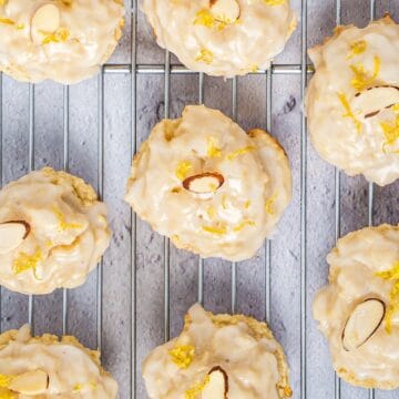 Italian lemon ricotta cookies on a wire rack with lemon glaze, sliced almond, and lemon zest.