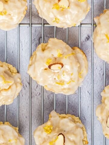Italian lemon ricotta cookies on a wire rack with lemon glaze, sliced almond, and lemon zest.