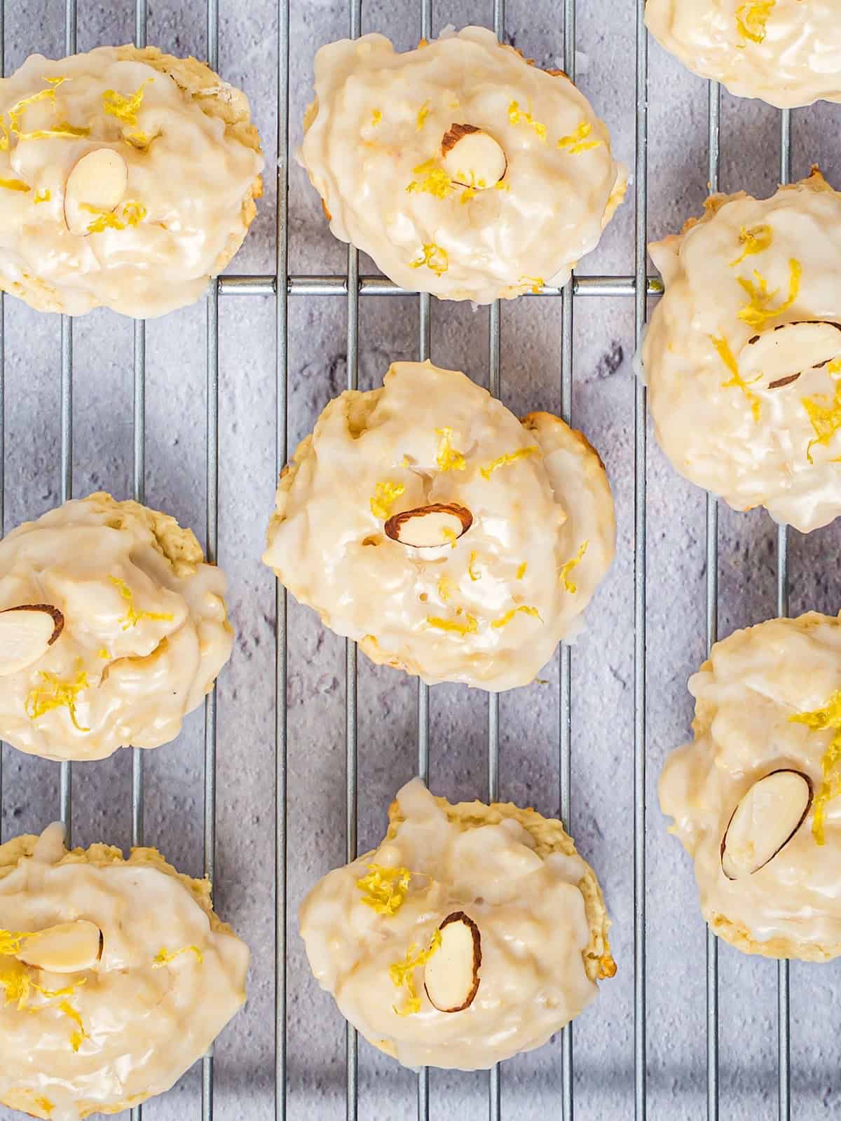 Italian lemon ricotta cookies on a wire rack with lemon glaze, sliced almond, and lemon zest.