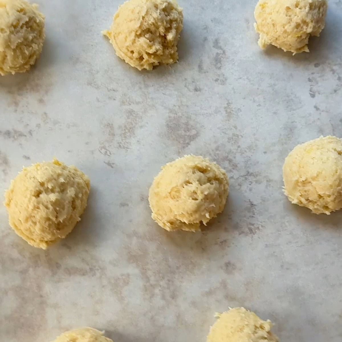 Lemon ricotta dough balls on a baking sheet with parchment.