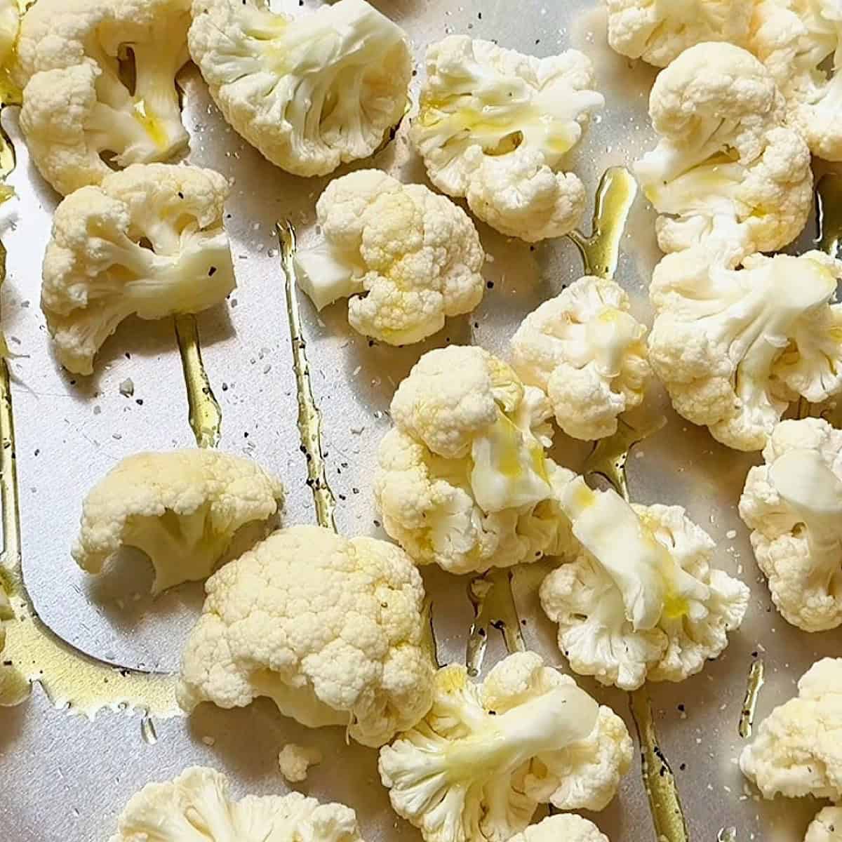 Olive oil drizzled over cauliflower with seasoning on a sheet pan.