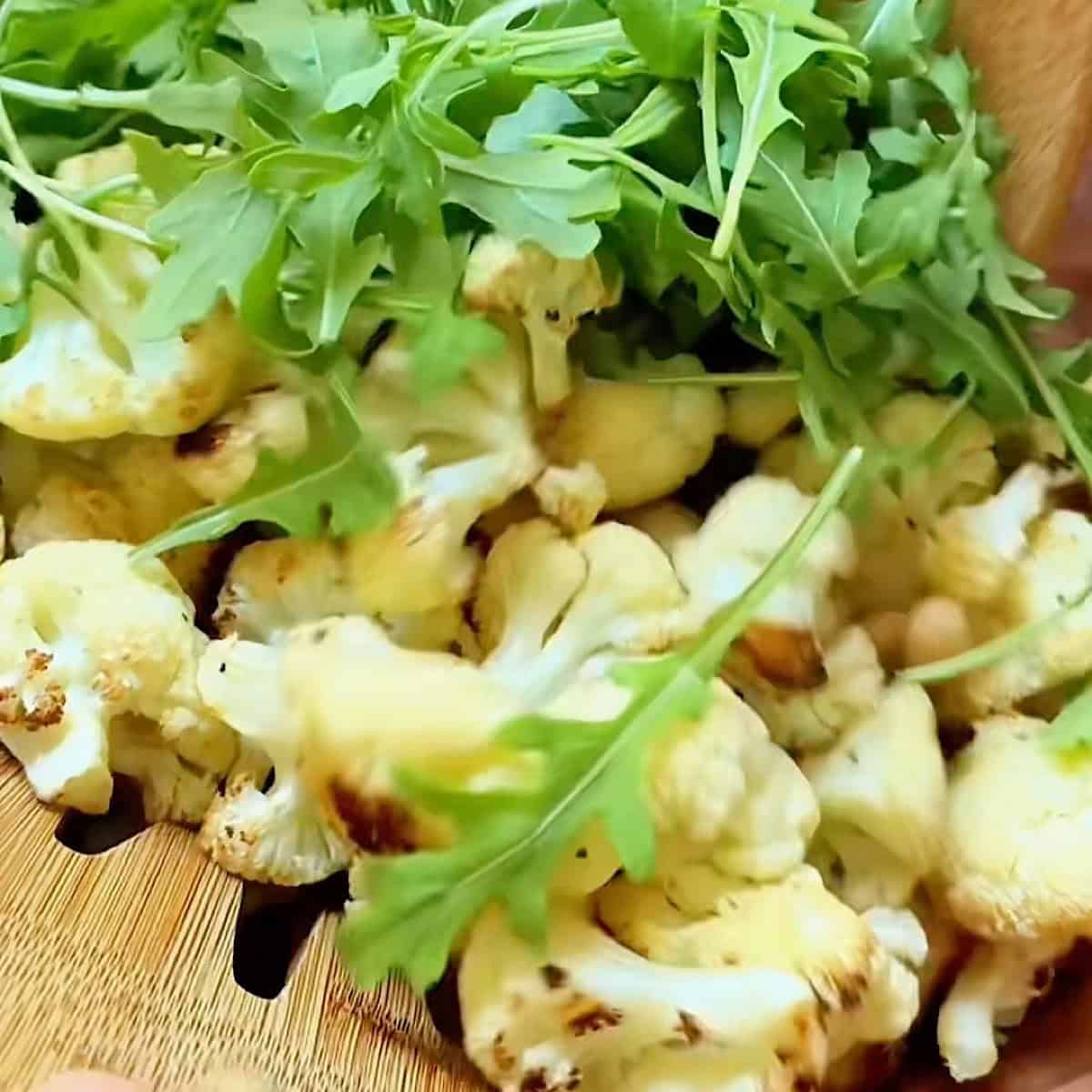 Tossing the warm cauliflower with cannellini beans and arugula in the dressing.