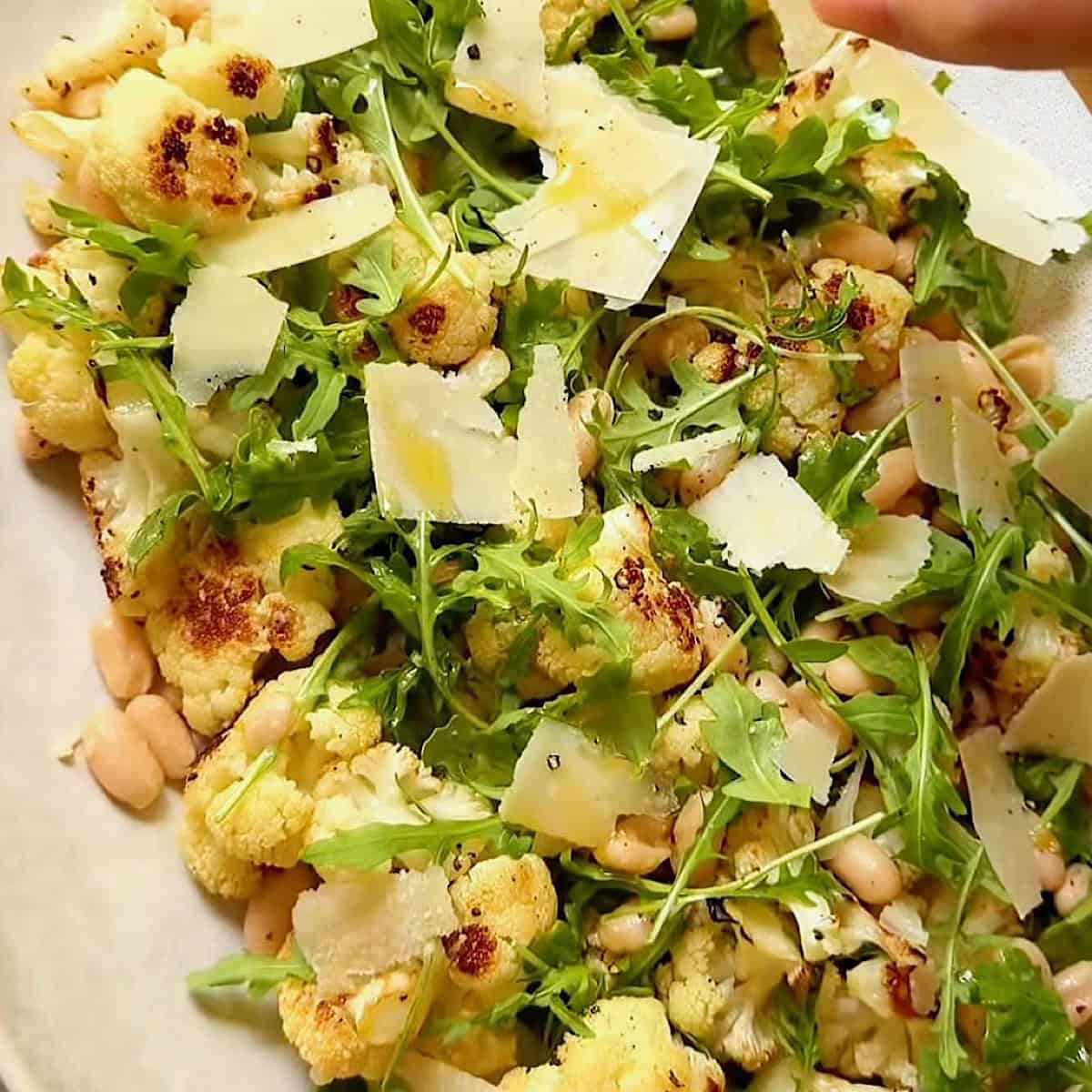 Warm cauliflower salad plated with shaved parmesan.