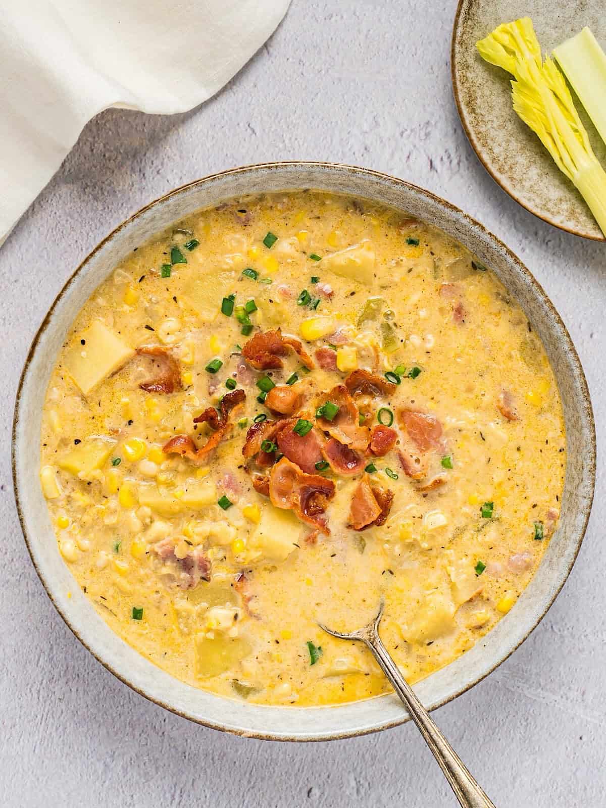 A bowl of creamy corn chowder with bacon and chive garnish next to a linen.