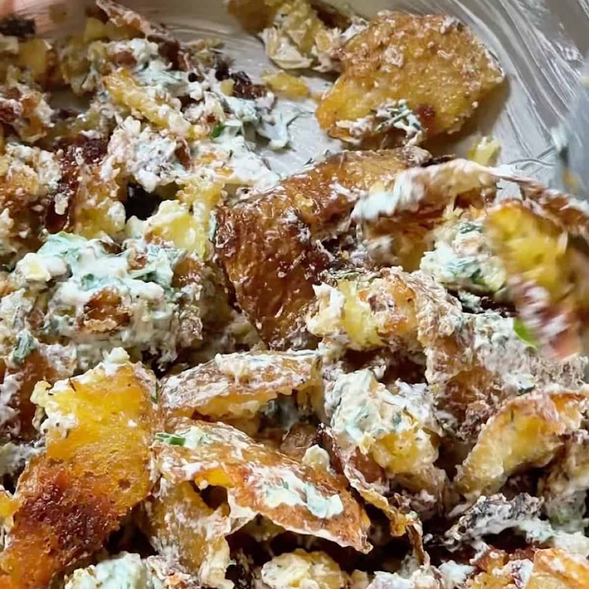 Smashed potato salad being tossed with the yogurt dressing.