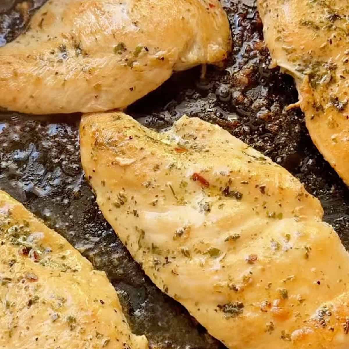 Four pieces of chicken breast searing in a skillet.