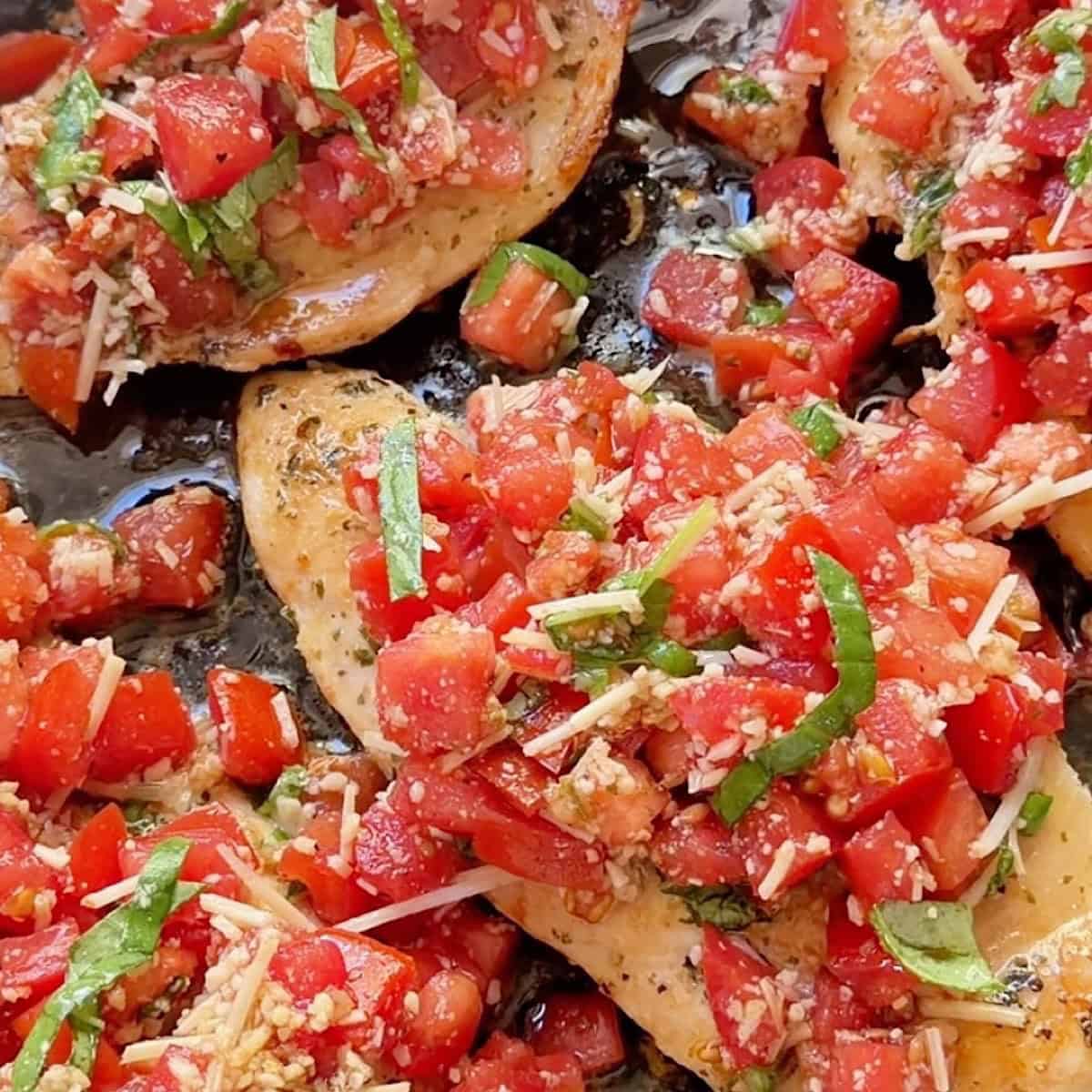 Browned and fully cooked chicken in a skillet with bruschetta topping.