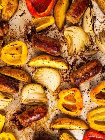 A full sheet pan showing the seasoned crispy browned edges of the sausage, potatoes, and peppers.