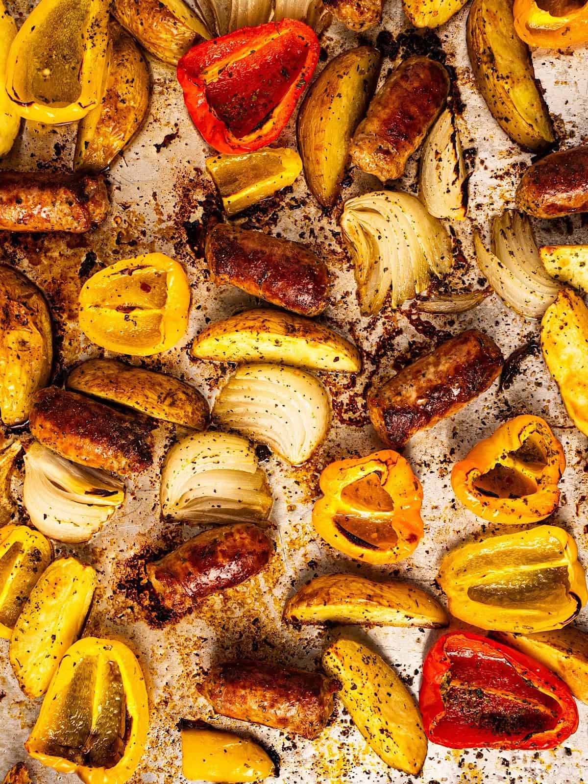 A full sheet pan showing the seasoned crispy browned edges of the sausage, potatoes, and peppers.