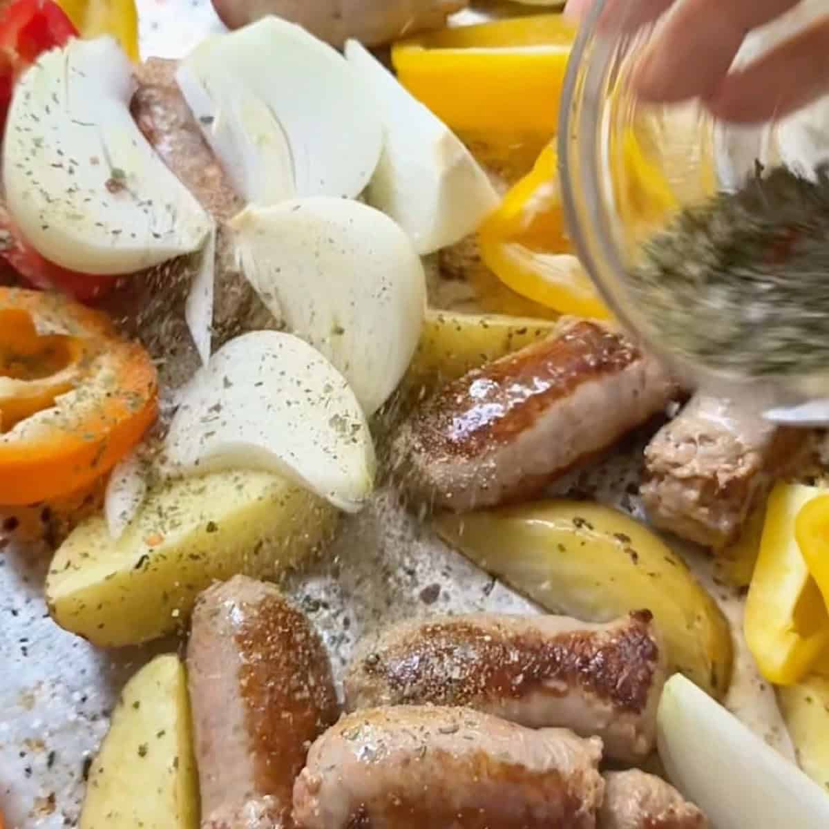 Seasoning the added sausage and vegetables on the sheet pan.