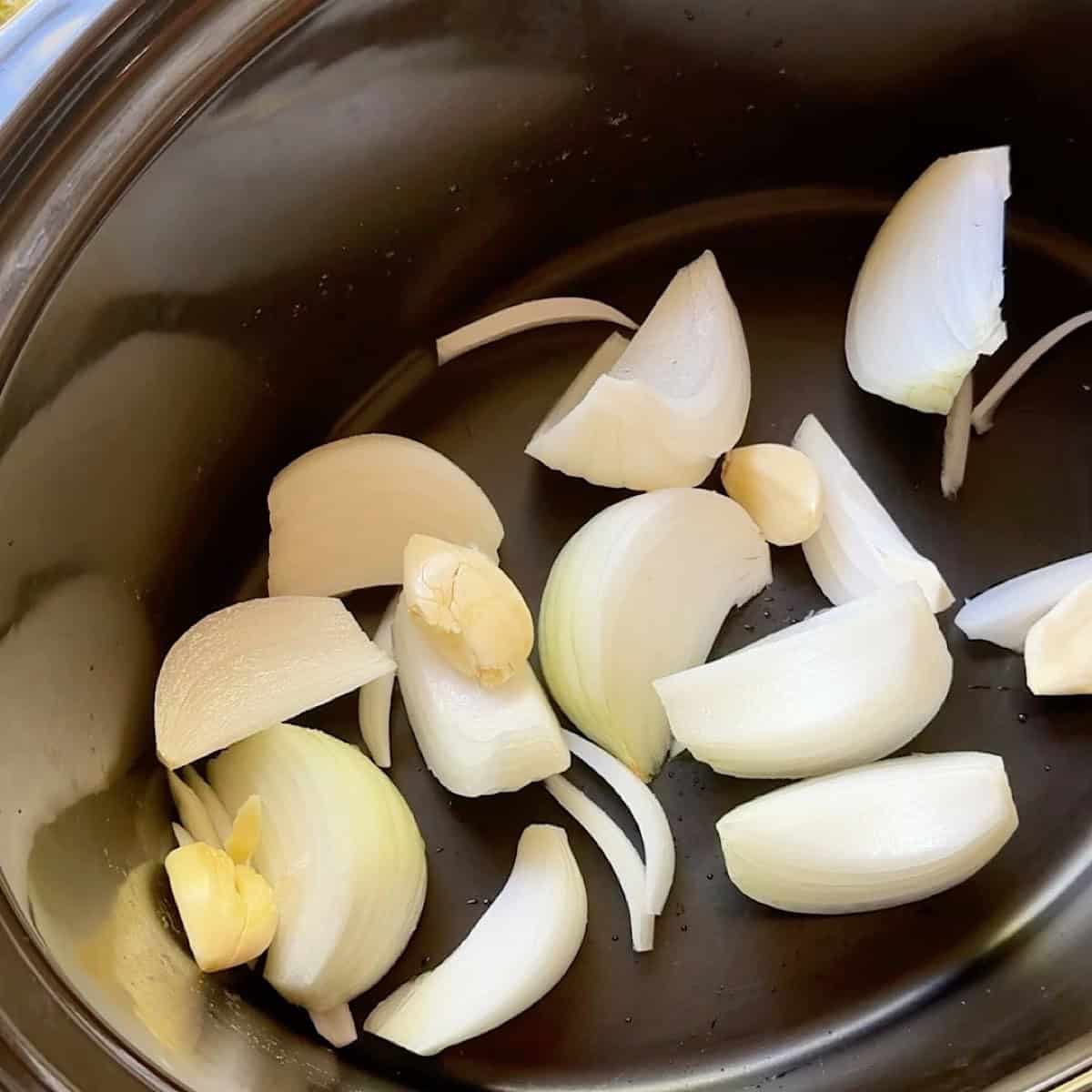 Onion wedges and smashed garlic spread out evenly in the bottom of the crockpot.