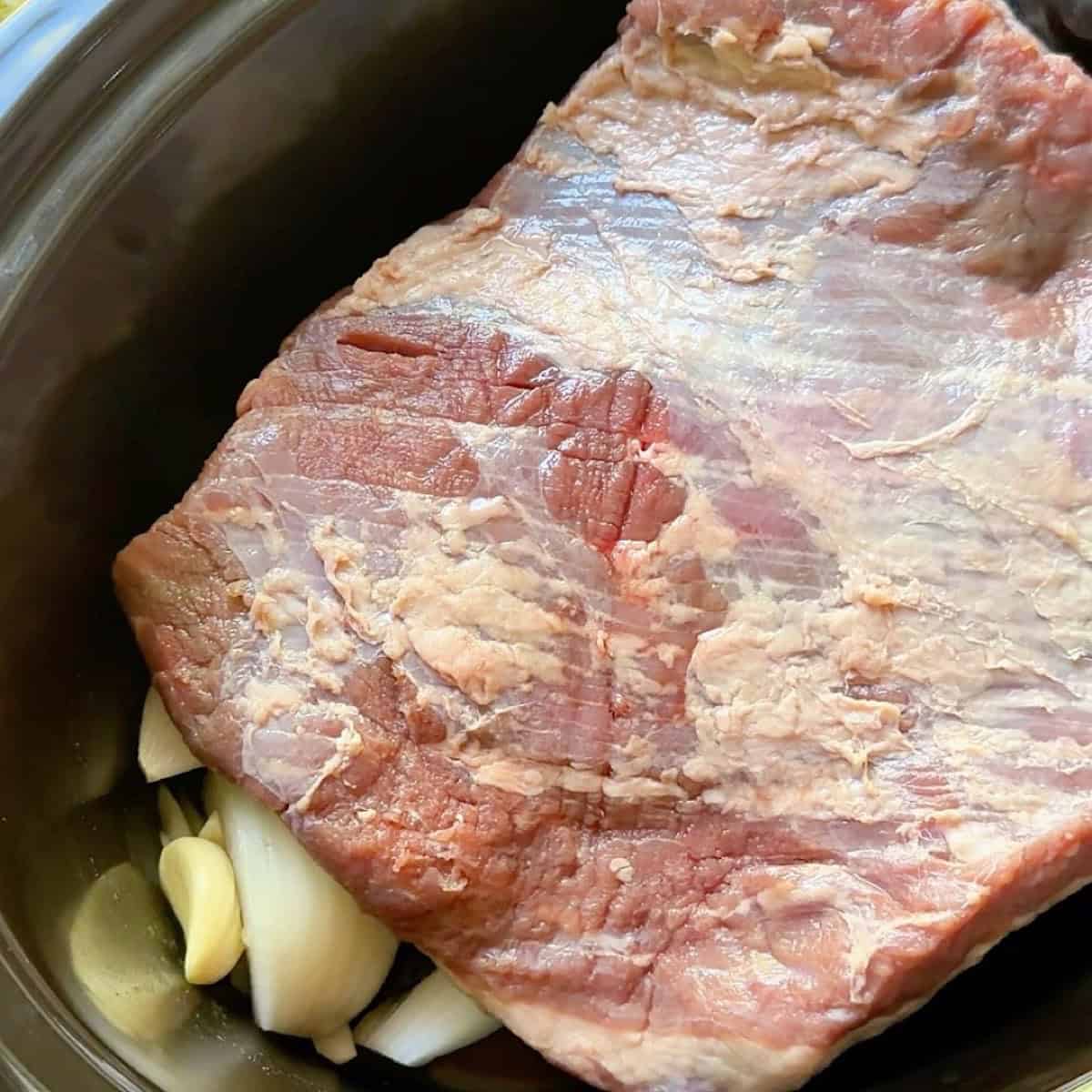 Trimmed beef brisket placed on top of onions.