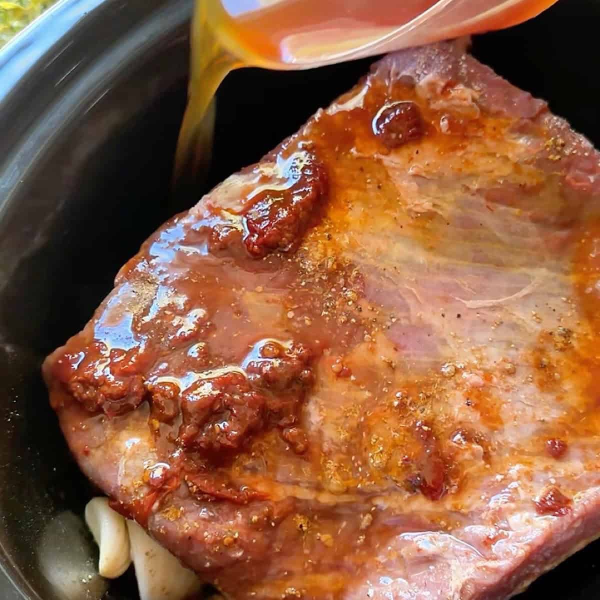 Pouring beef broth around the seasoned brisket in the slow cooker.