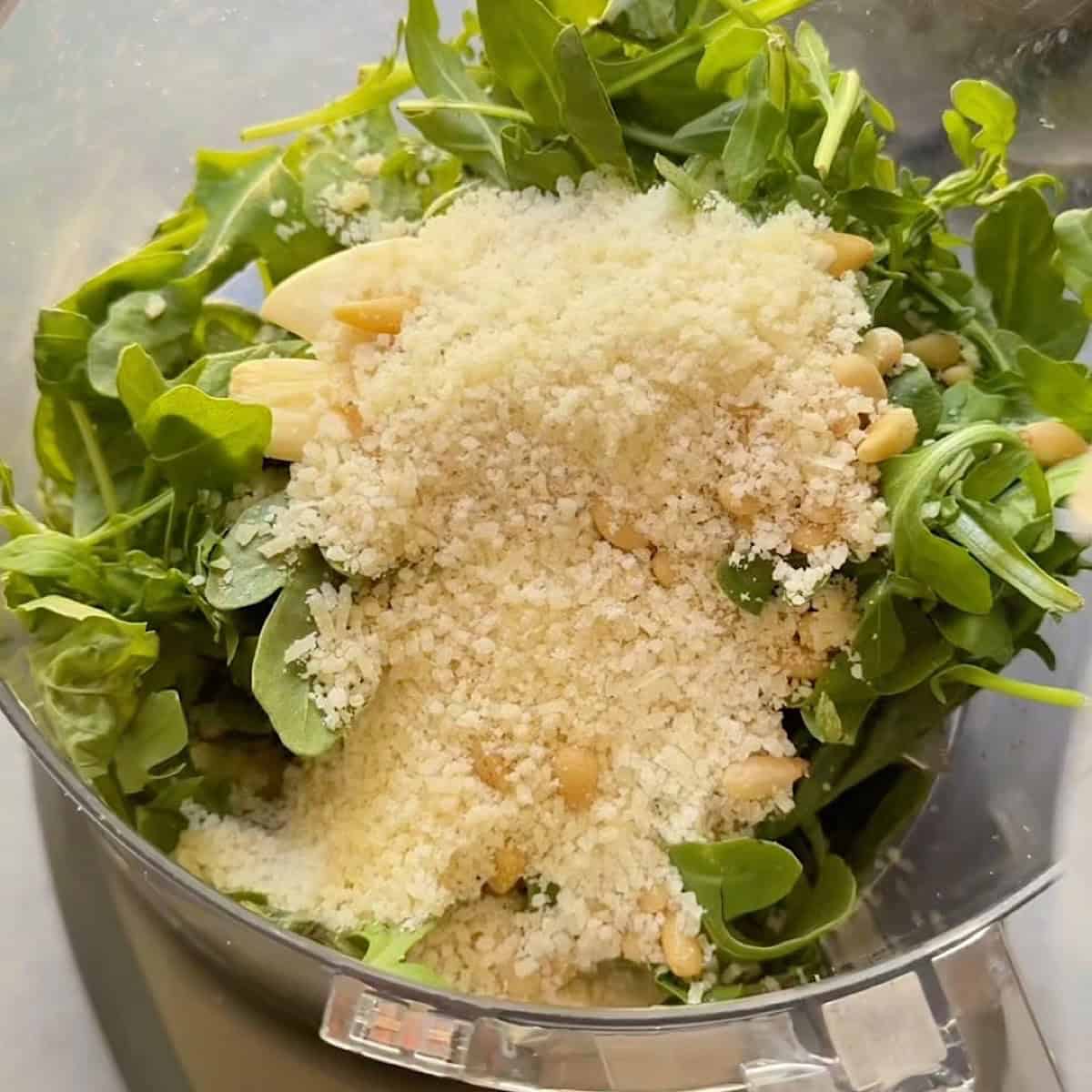 Basil, arugula, parmesan cheese, pine nuts, and garlic in a food processor.