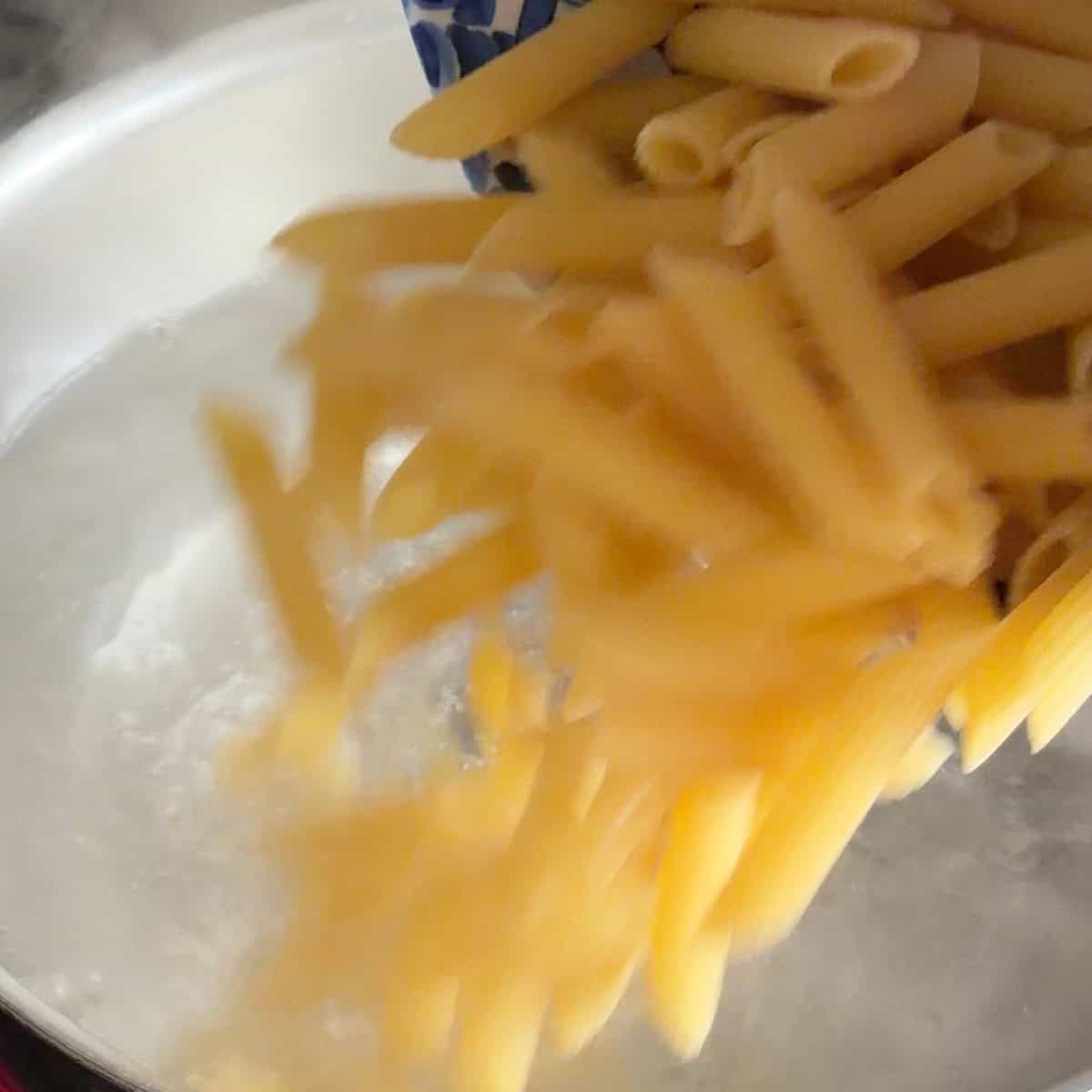 Pouring ziti pasta into boiling water.