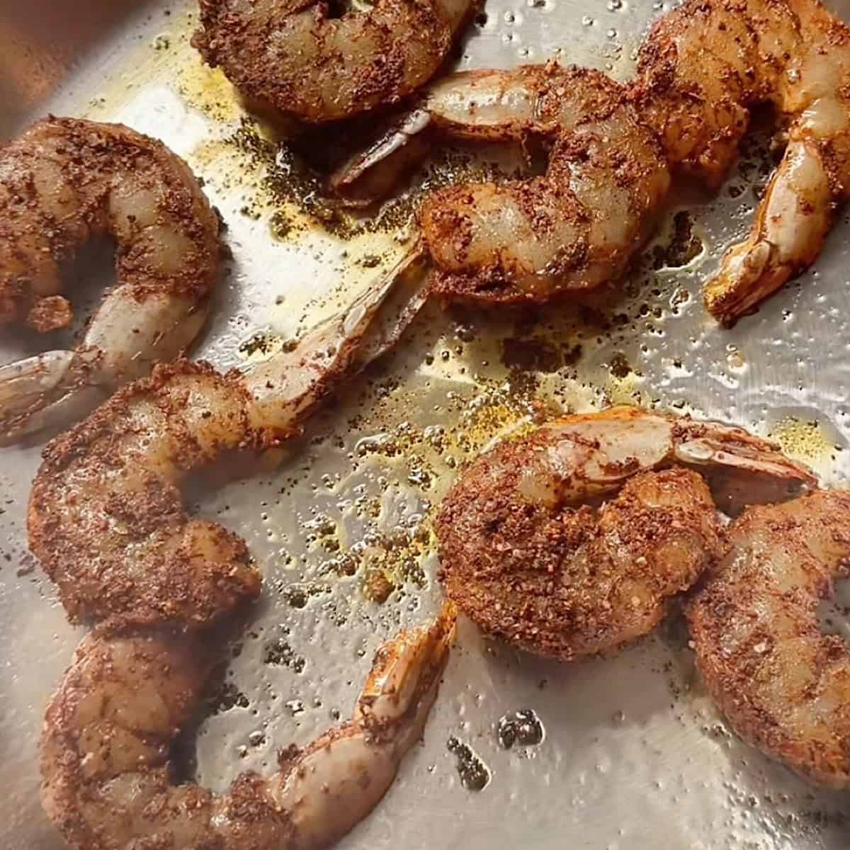 Blackened shrimp cooking in a skillet with oil.