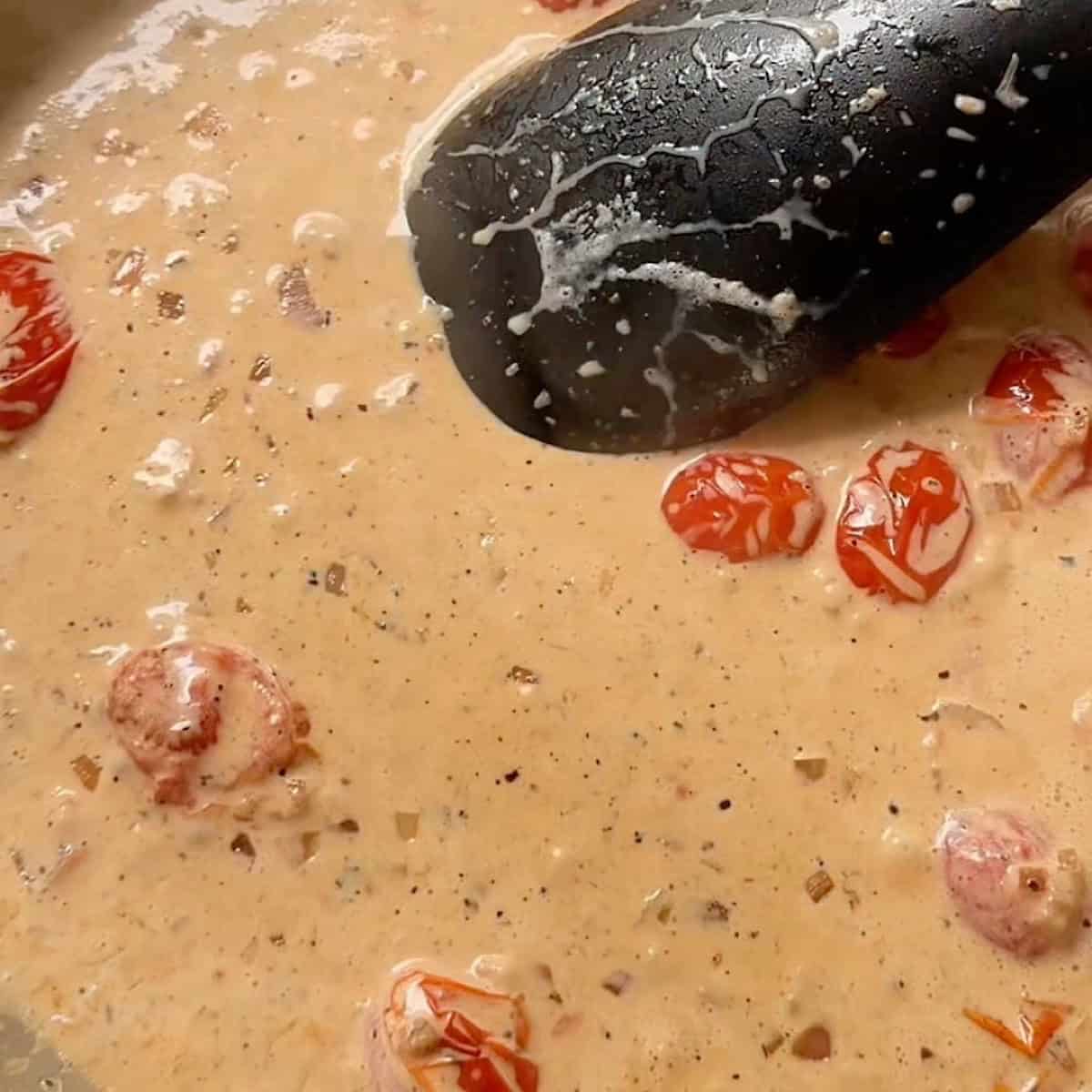 Creamy cajun sauce with blistered tomatoes being stirred.