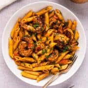 Creamy blackened shrimp pasta with garnish in a white bowl plated next to linen and wooden box.