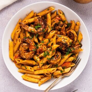 Creamy blackened shrimp pasta with garnish in a white bowl plated next to linen and wooden box.