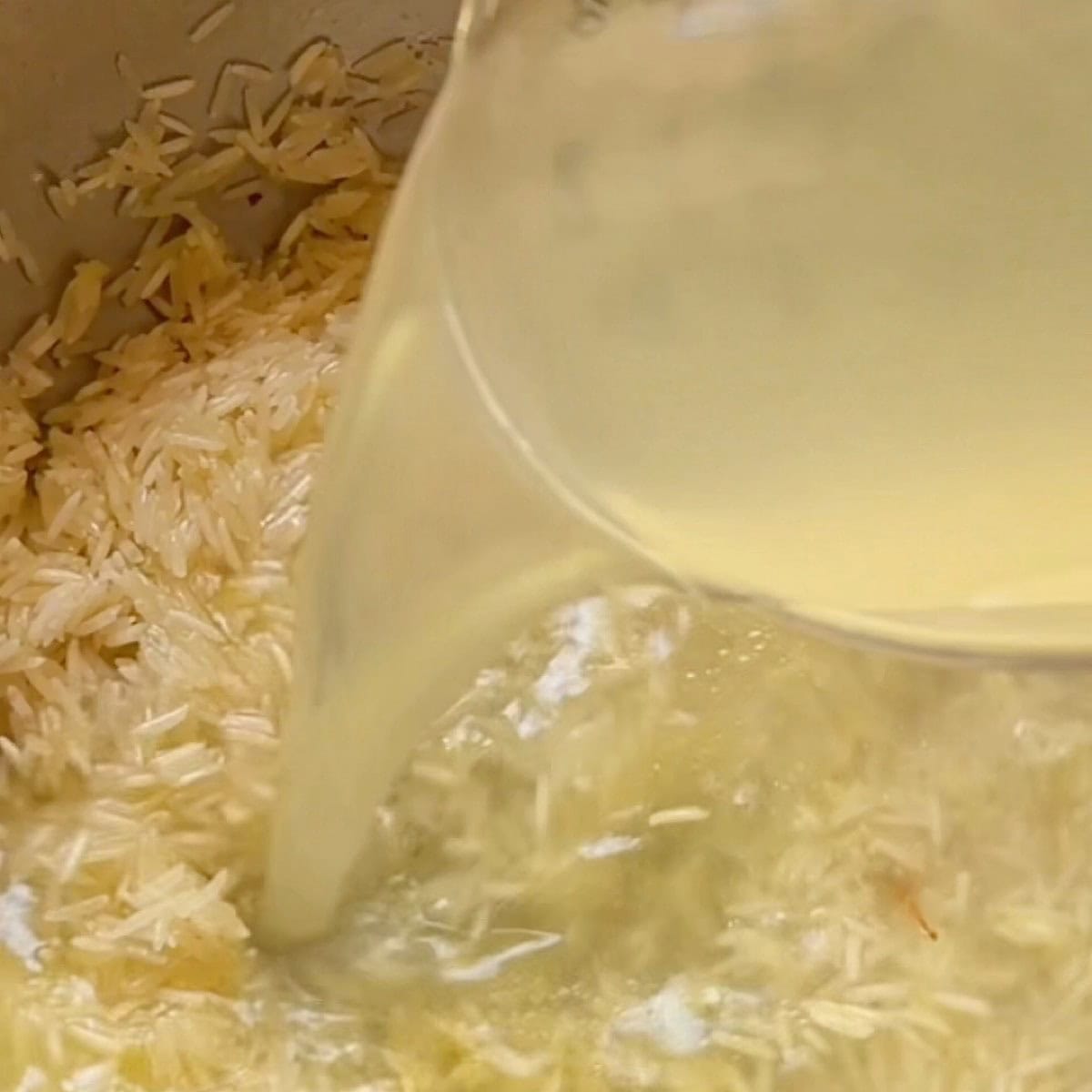 Adding chicken broth to the basmati rice.