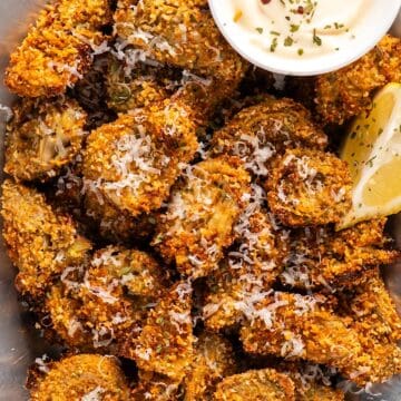 A platter of crispy artichoke hearts with lemon wedges, parmesan garnish, and a small bowl of garlic aioli.